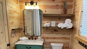Une petite salle de bain en bois comprenant un lavabo, un miroir, des toilettes et un espace pour ranger les serviettes.
