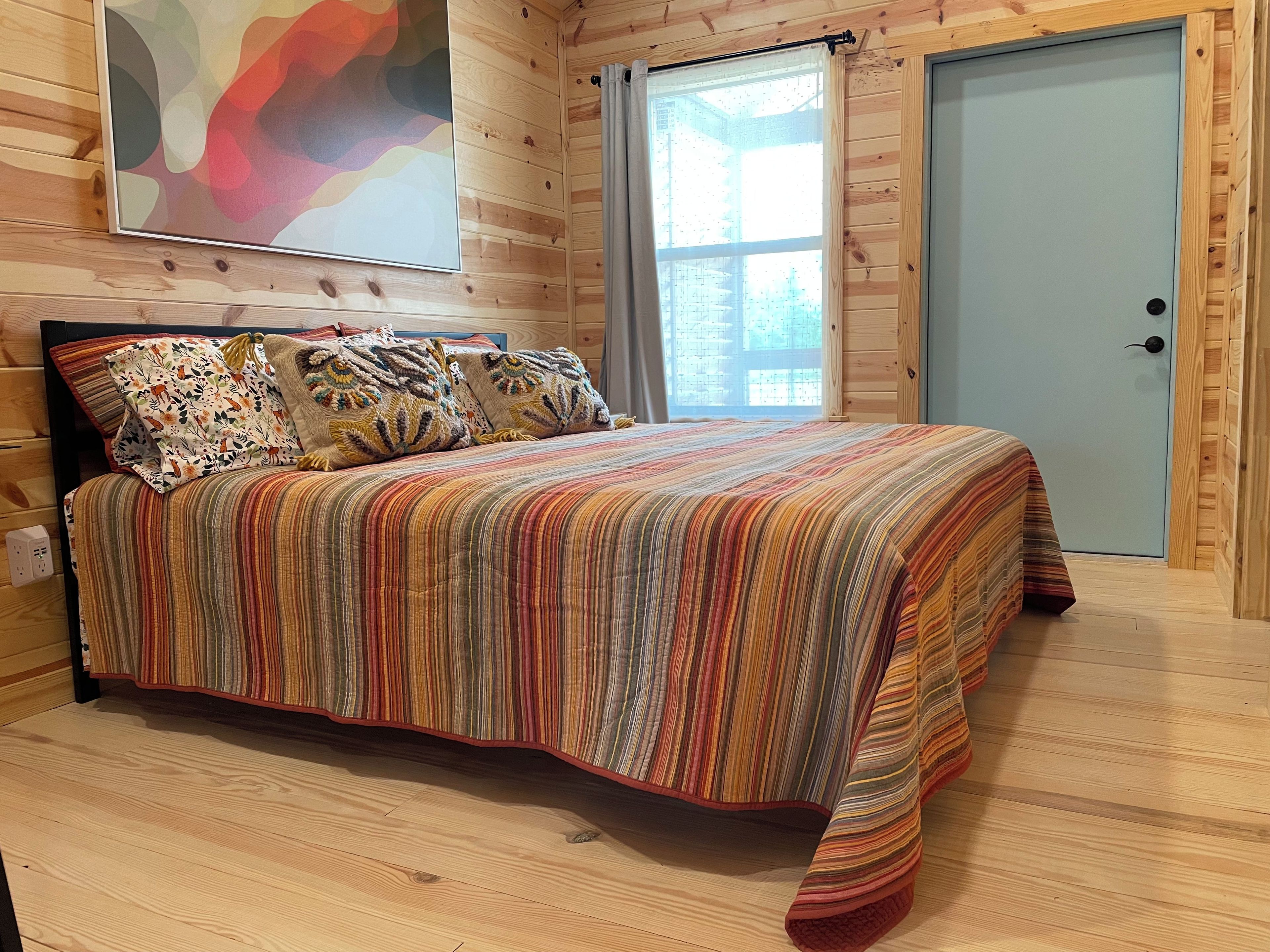 A wooden-paneled room with a bed, a door, and a window.