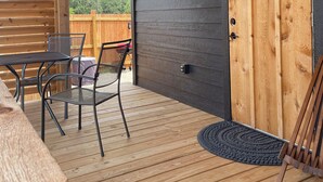 Une terrasse couverte avec une plateforme en bois, des meubles en métal et une porte donnant sur un espace extérieur.