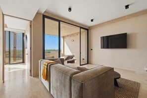 A modern living room with a sofa, a TV mounted on the wall, and a view through a glass door. - Sáasil: Tranquil Oasis w/ Golf course views (Playa del Carmen)