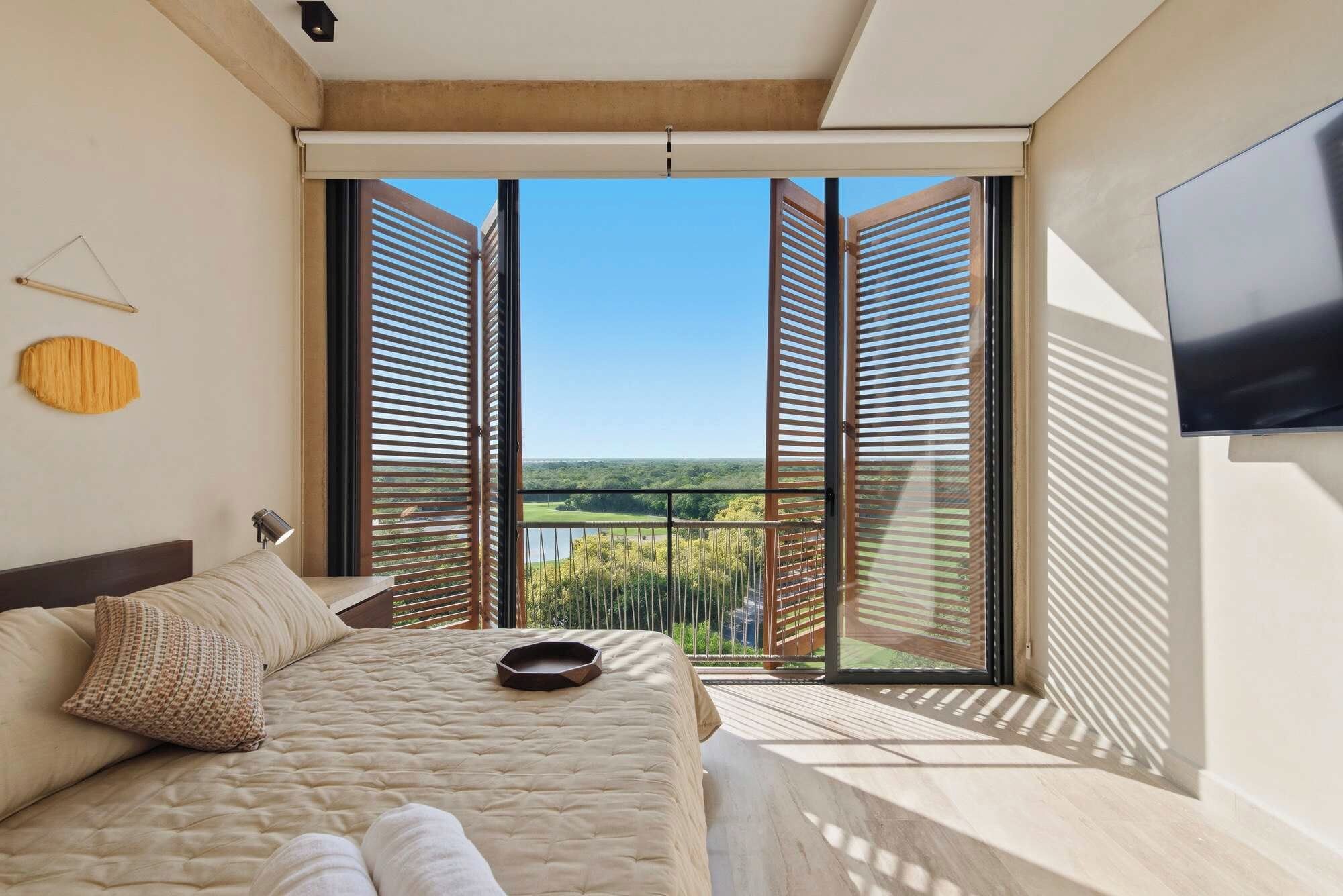 A bedroom with a large bed, a flat-screen TV, and a balcony with open shutters.