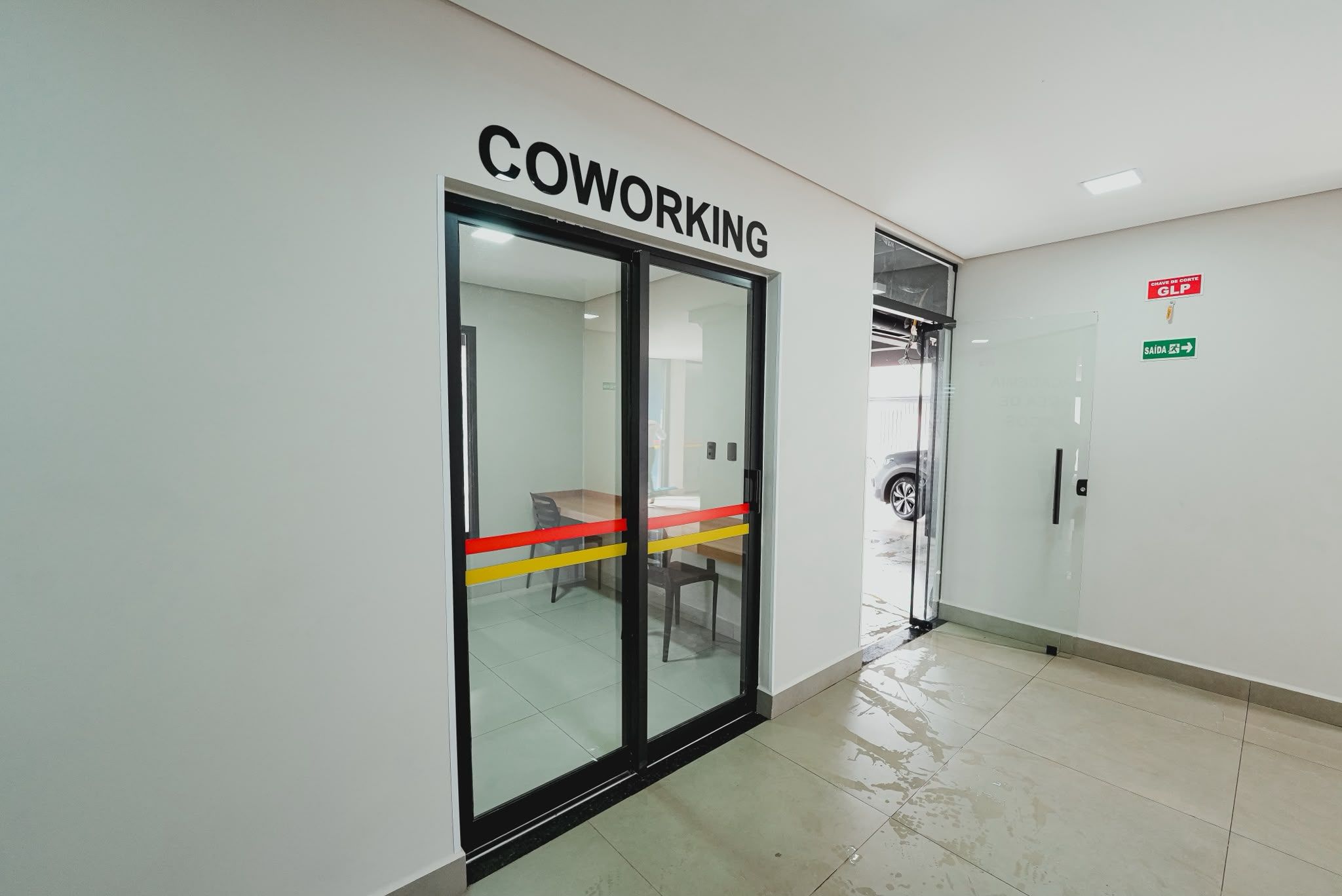 Käytävällä on lasiovi, jossa on kyltti, jossa lukee ”COWORKING”, ja toinen kyltti, joka osoittaa uloskäynnin.