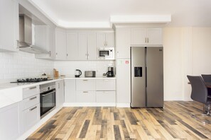 A modern kitchen with white cabinetry, a stainless steel refrigerator, a microwave, a coffee maker, and a gas stove. - TenoHomes Spacious Buenavista House & BBQ (Buenavista del Norte)