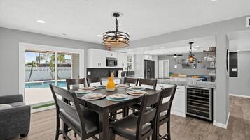 A modern kitchen with white cabinets, a dining area with a table set for four, and a pool visible through the glass door.