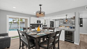 Une cuisine moderne avec des meubles blancs, un coin repas avec une table dressée pour quatre personnes, et une piscine visible à travers la porte vitrée.