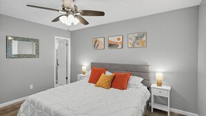 Une chambre à coucher avec un lit, un ventilateur de plafond, une table de chevet avec une lampe et des œuvres d’art accrochées au mur.