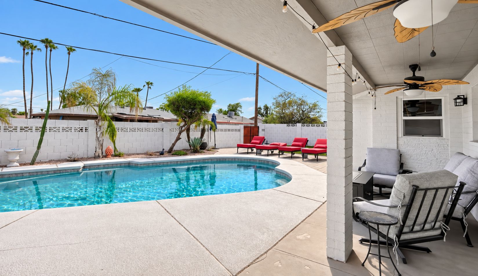 A swimming pool with a patio area, lounge chairs, and a ceiling fan.