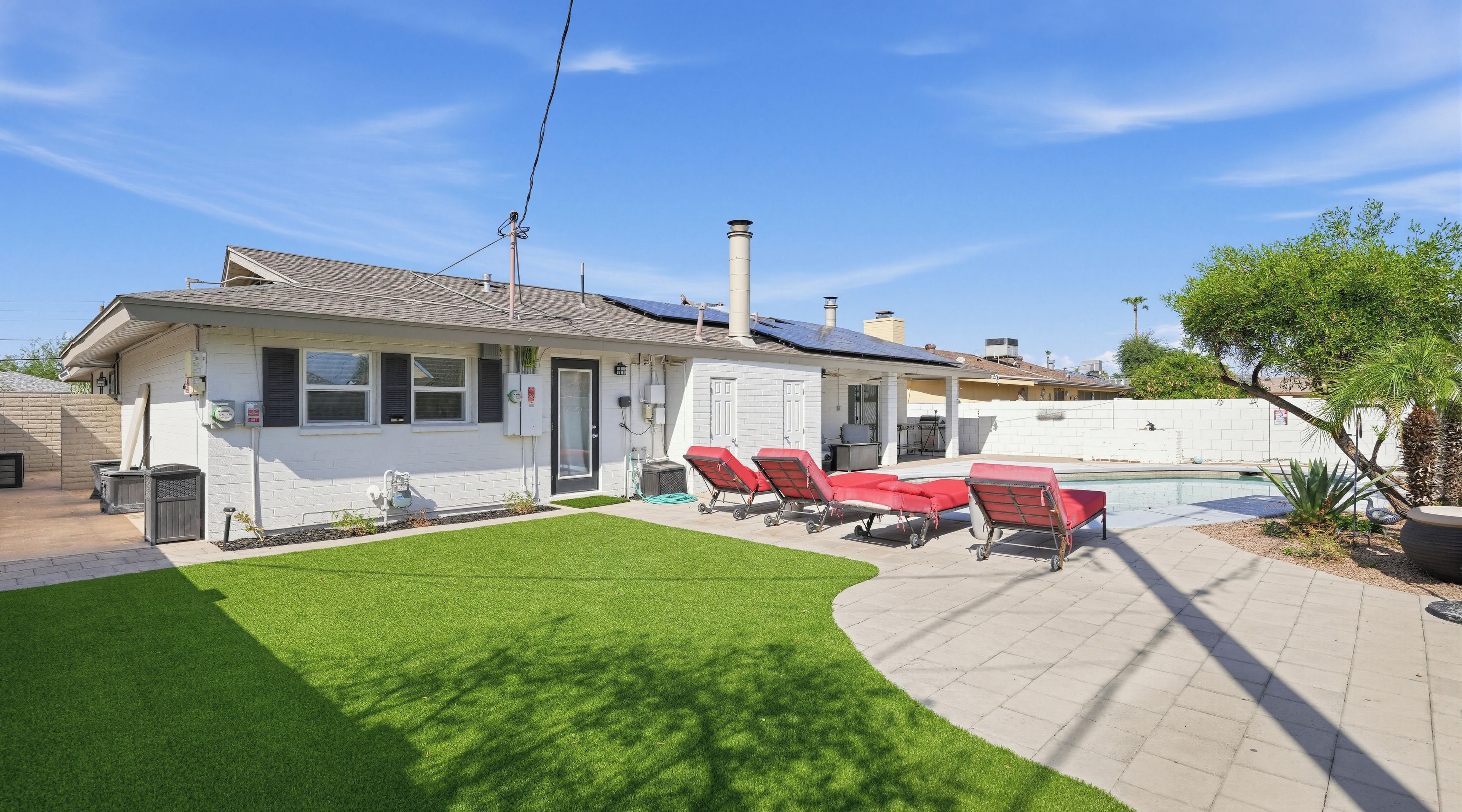 A residential property with a swimming pool, a patio with red lounge chairs, and a well-maintained lawn.