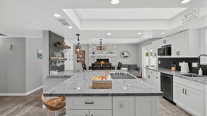A modern kitchen with a central island, white cabinetry, and a dining area with a sofa and table.