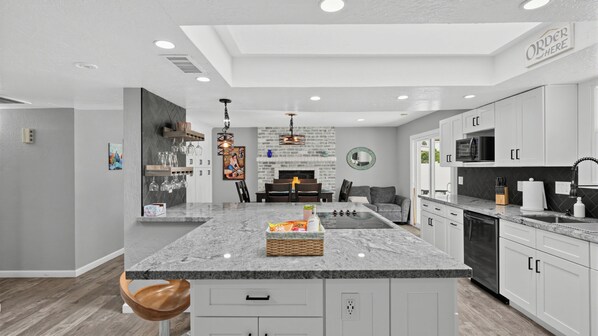 A modern kitchen with a central island, white cabinetry, and a dining area with a sofa and table.