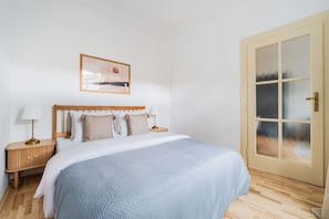 A bedroom with a bed, bedside tables, a wall-mounted picture, and a door with frosted glass panels. - Blueground | Vinohrady, view, nr park &  Náměstí Míru (PRG-112) (Prague)
