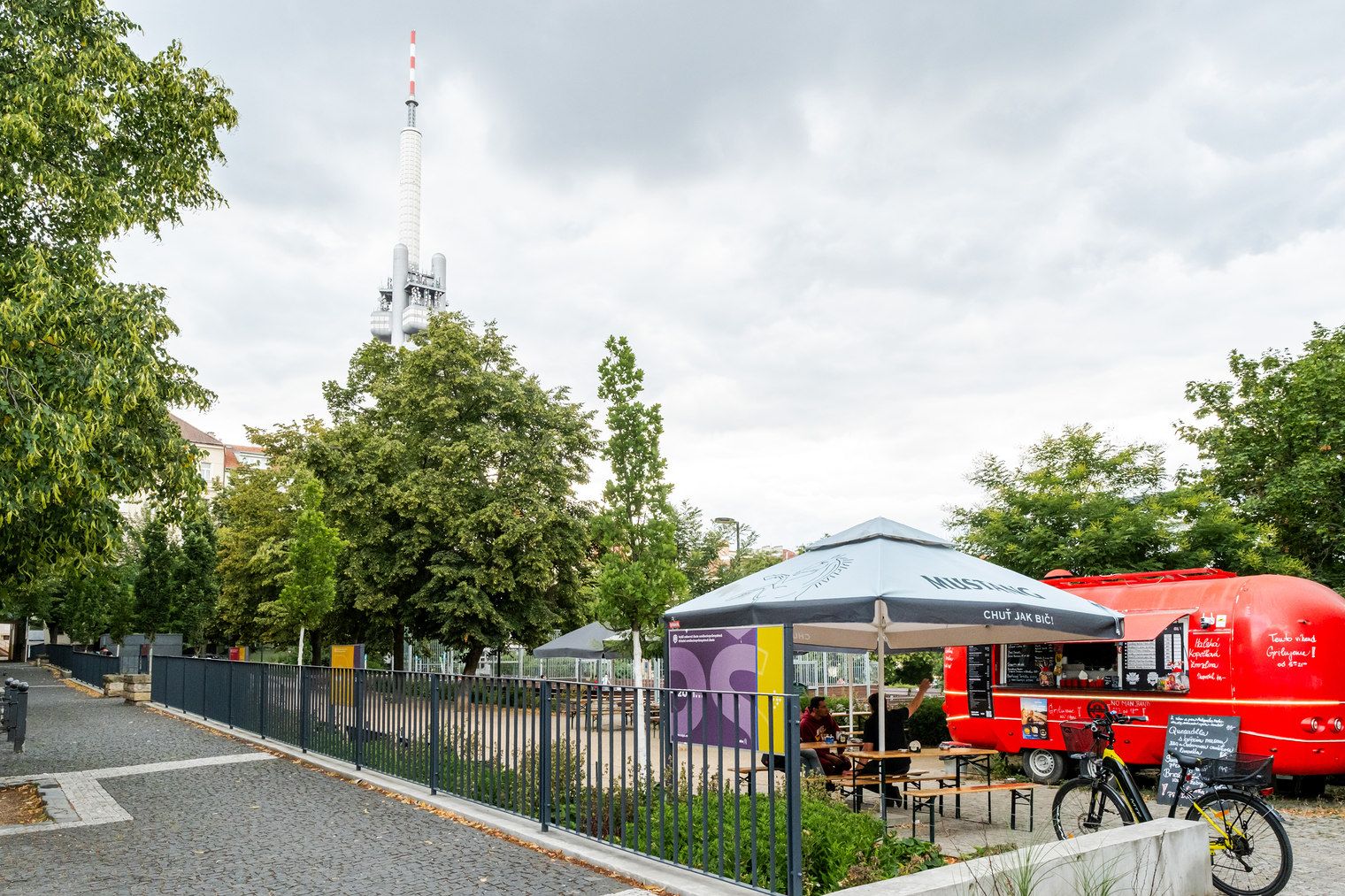 Un puesto de comida callejera con una carpa, una bicicleta y un camión de comida rojo al fondo.