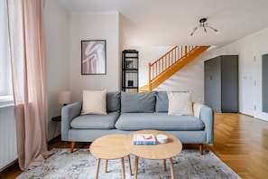 A modern living room with a grey sofa, two wooden side tables, a staircase, and a framed abstract artwork on the wall. - Blueground | Vinohrady, balcony, nr Riegrovy Sady (PRG-116) (Prague)