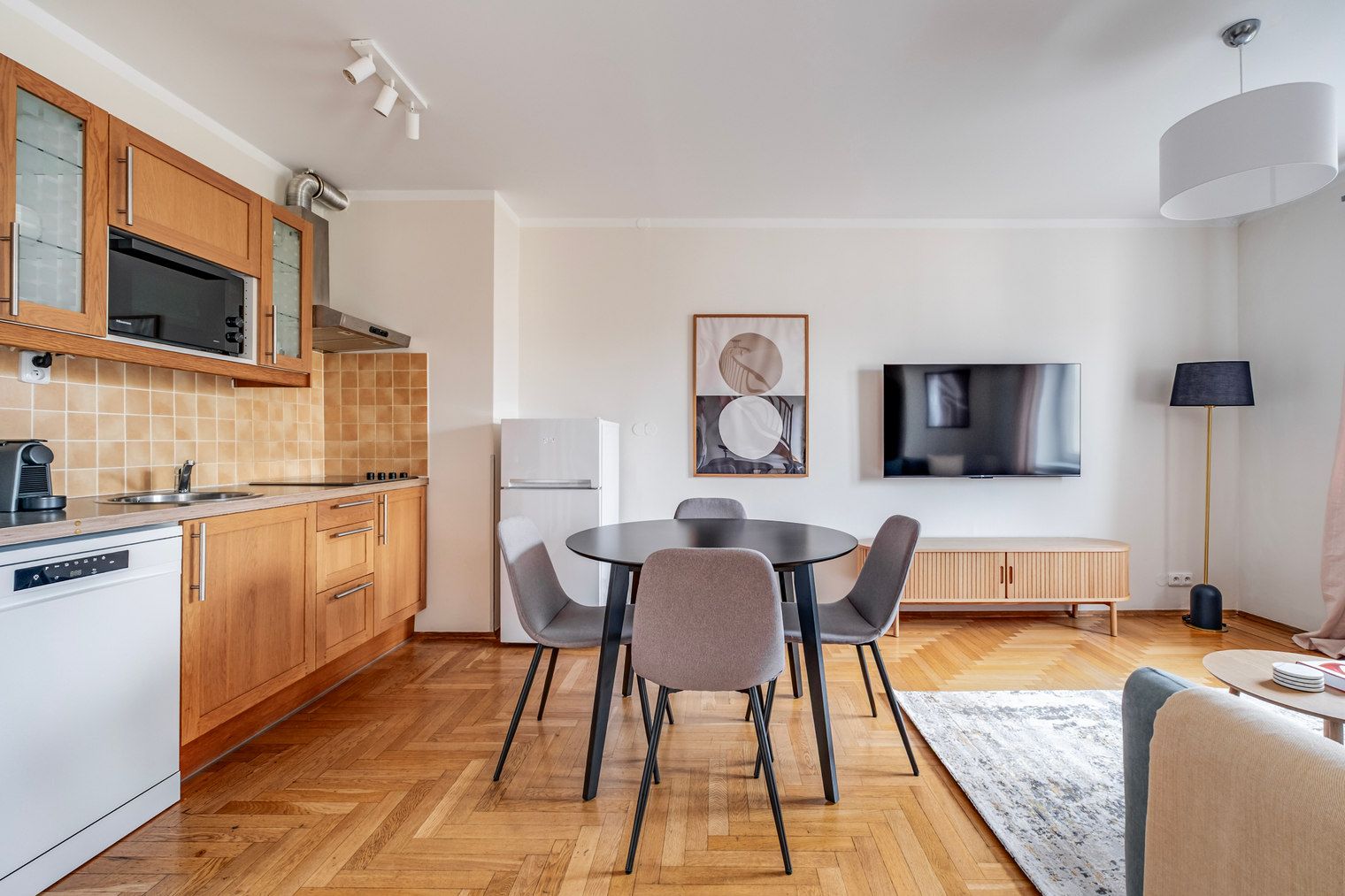 A modern kitchen with wooden cabinets, a built-in microwave, and a dining area with a round table and chairs.