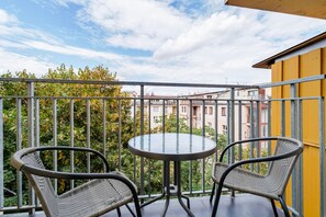 Ein Balkon mit rundem Tisch und zwei Korbstühlen, mit Blick auf ein Wohngebiet mit Gebäuden und Bäumen.