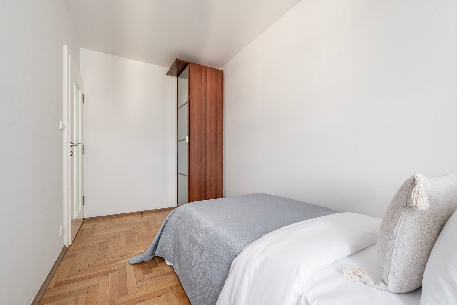 Een slaapkamer met een bed, een houten kledingkast en een visgraatvloer.