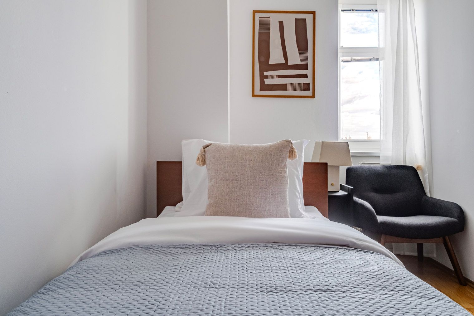 A hotel room with a bed, a chair, a lamp, and a painting on the wall.