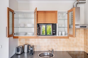 A kitchen with open wooden cabinets, a stainless steel sink, and a view of greenery outside. - Blueground | Vinohrady, balcony, nr Riegrovy Sady (PRG-116) (Prague)