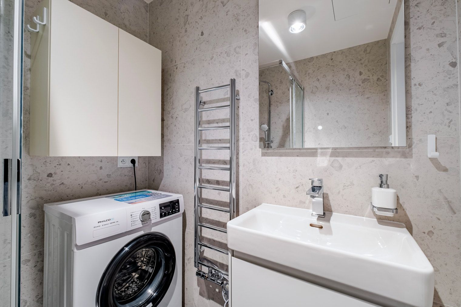 Une salle de bain moderne équipée d’un lave-linge, d’un évier, d’un miroir et d’un porte-serviettes.