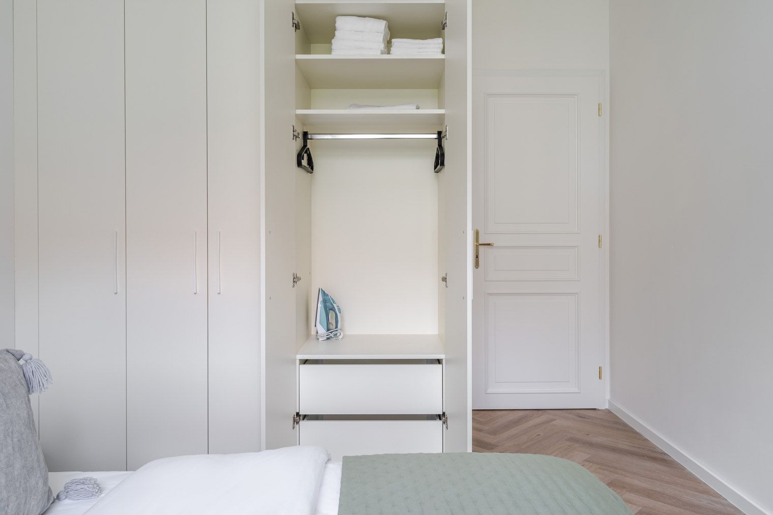 A bedroom with a bed, a wardrobe with hanging space, and a door.