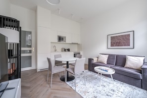 Ein modernes Wohnzimmer mit einem grauen Sofa, einem runden Couchtisch und einem Essbereich mit weißem Tisch und Stühlen.