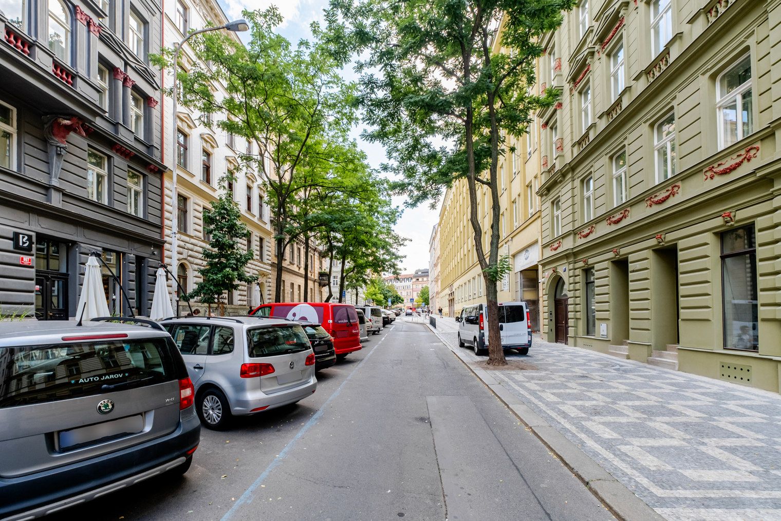 Eine Straße mit parkenden Autos und Bäumen, gesäumt von Gebäuden.