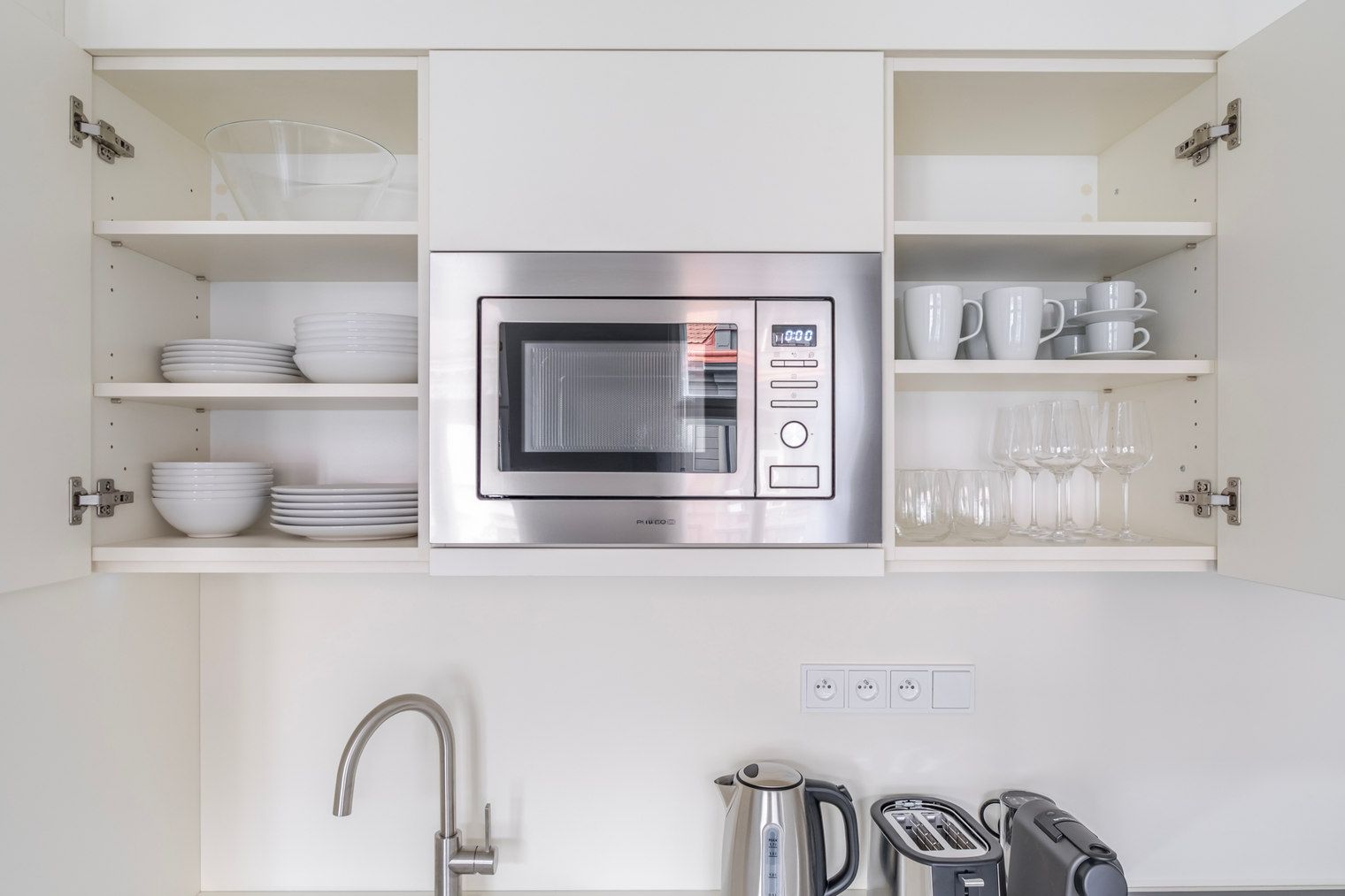 Una cocina moderna con microondas integrado, electrodomésticos de acero inoxidable y armarios blancos.