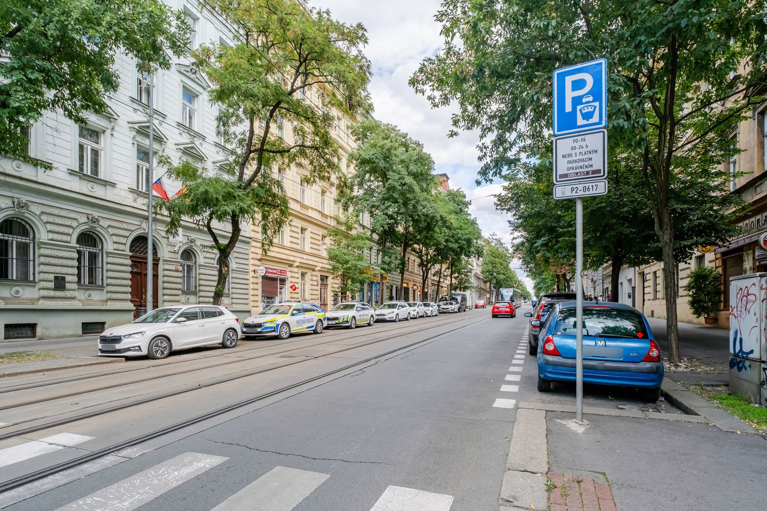Een straat met tramrails, geparkeerde auto's en een blauw parkeerbord.