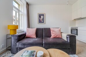 A modern living room with a sofa, a coffee table, and a kitchen area with cabinets and an oven. - Blueground | Vinohrady, view, nr Riegrovy sady (PRG-122) (Prague)