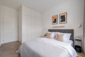 A bedroom with a bed, white wardrobe, and two framed pictures on the wall. - Blueground | Vinohrady, view, nr Riegrovy sady (PRG-122) (Prague)