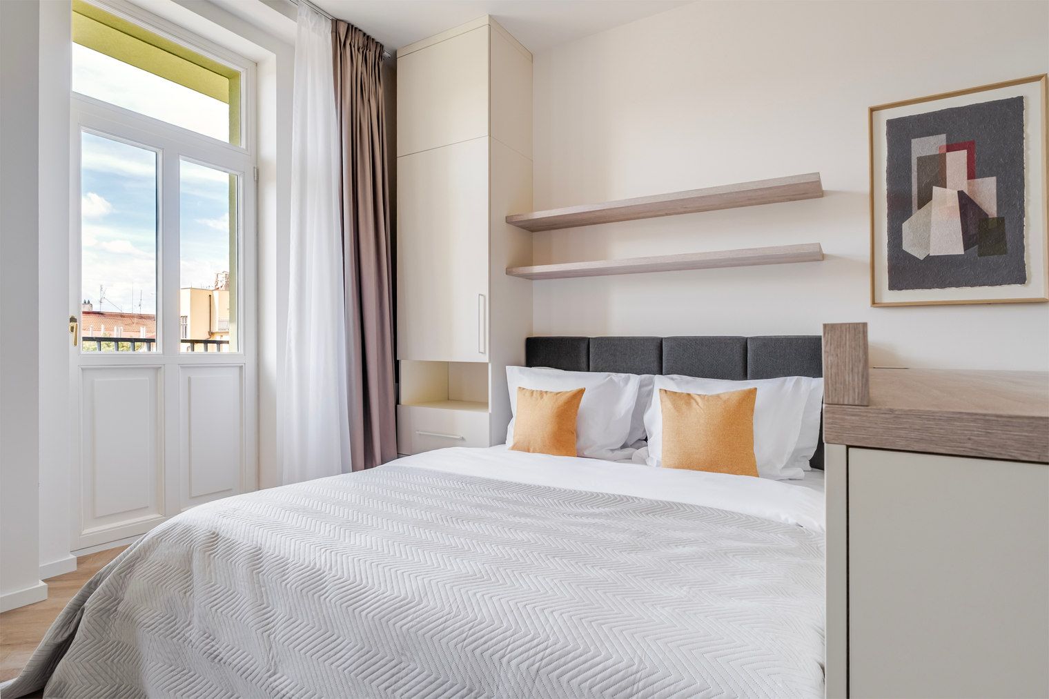 Una habitación de hotel con una cama, una ventana con cortinas, un cabecero y una repisa en la pared.