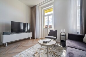 A modern living room with a flat-screen TV, a grey sofa, a round coffee table, and a window with curtains. - Blueground | Vinohrady, view, nr Riegrovy Sady (PRG-124) (Prague)