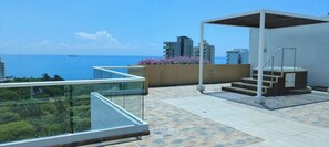 A rooftop terrace with a glass balustrade, a hot tub, and a view of the sea. - Modern condo, 5-min walk to the beach · Pools, Gym & Coworking (Santa Marta)