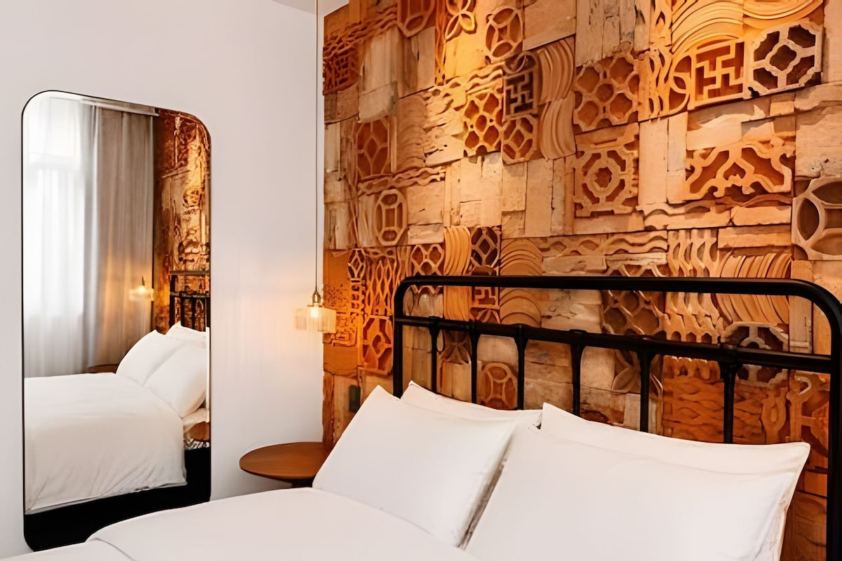 A hotel room with a bed, a nightstand, a mirror, and a wall with intricate wood carvings.