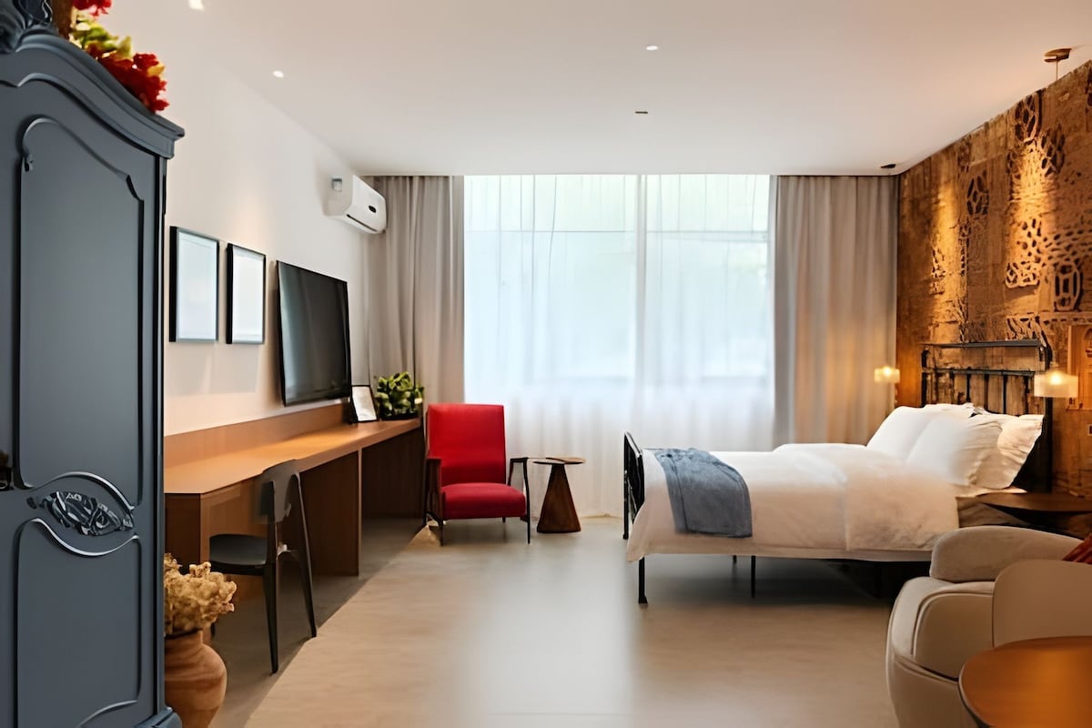 A hotel room with a bed, a desk, a chair, a TV, and a decorative wall.