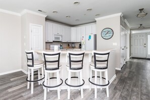 A kitchen with white cabinets, a microwave, a refrigerator, and a clock on the wall. - Sunset Island 37 Fountain Drive West, Unit 3E (Ocean City)