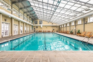 An indoor swimming pool with a high ceiling and skylights, surrounded by lounge chairs and a tiled floor. - Sunset Island 37 Fountain Drive West, Unit 3E (Ocean City)