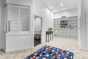 A hallway with a patterned rug, a bed, a small table with a plant, and a bookshelf. - Large Waterfront Stay by Britomart & Harbour (Auckland)