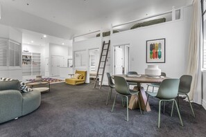 A modern living room with a sofa, a yellow armchair, a dining table with chairs, and a ladder. - Large Waterfront Stay by Britomart & Harbour (Auckland)