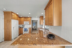 A kitchen with wooden cabinets, a white refrigerator, a microwave, a stove, and a granite countertop.