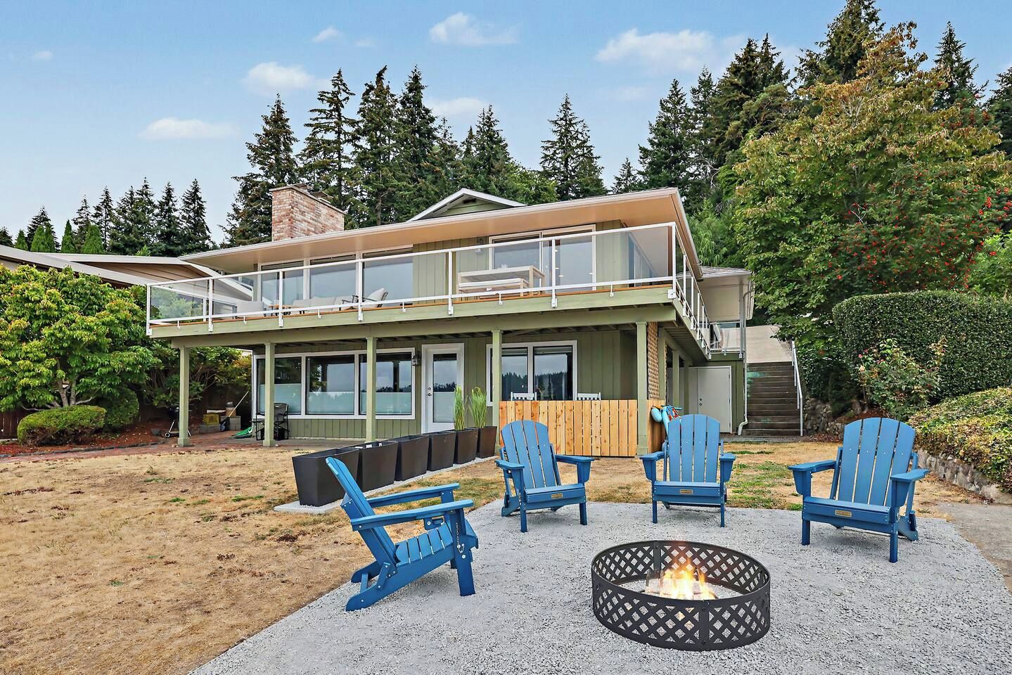 Ein zweistöckiges Haus mit einer Terrasse, Sitzgelegenheiten im Freien und einer Feuerstelle.