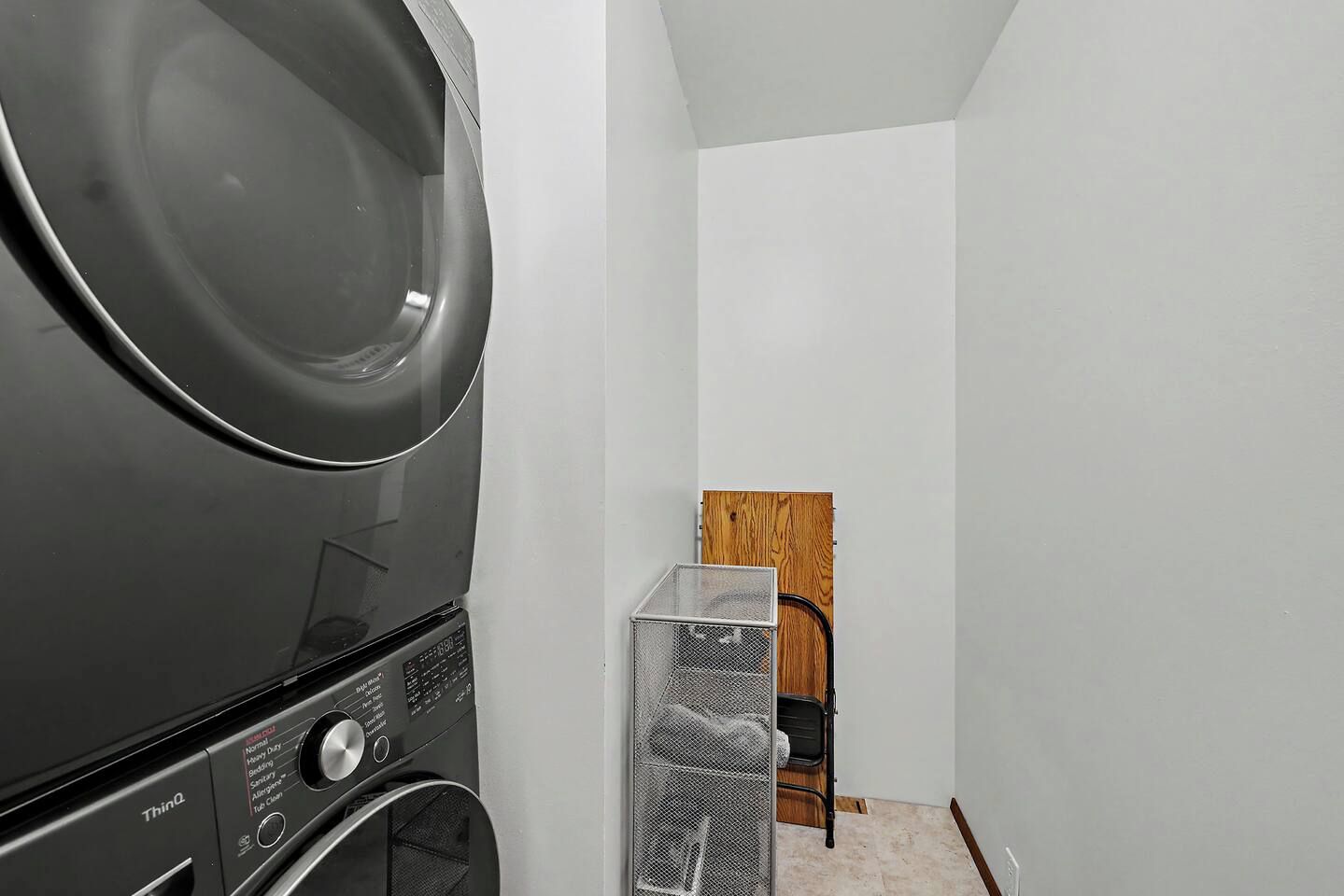 A laundry area with a stacked washer and dryer, a metal drying rack, and a wooden door.