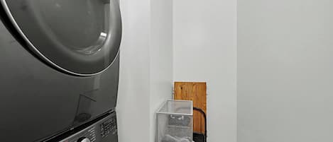 A laundry area with a stacked washer and dryer, a metal drying rack, and a wooden door.
