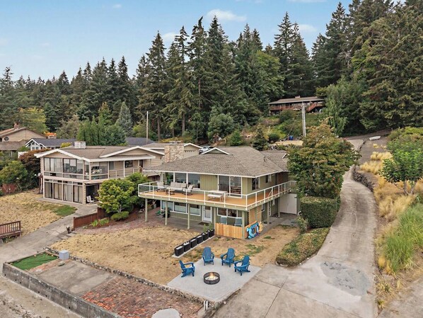 A two-story house with a deck, outdoor seating, and a fire pit.