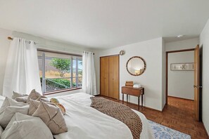 Un dormitorio con cama, mesita de noche, espejo, armario y vistas al exterior.