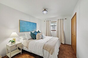 A bedroom with a bed, bedside table, lamp, and a painting on the wall.
