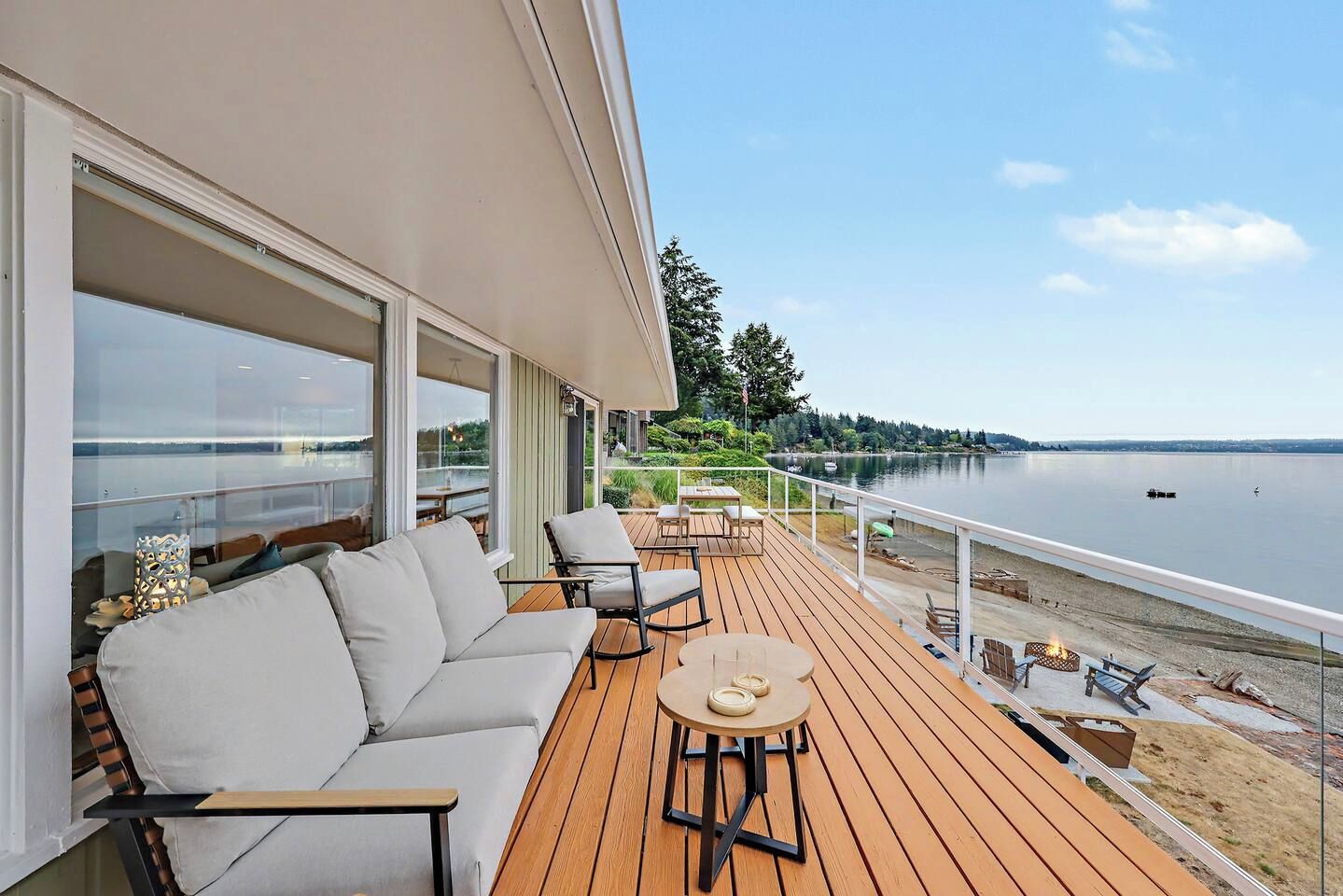 A deck with a sofa, chairs, and a table, overlooking a calm body of water.