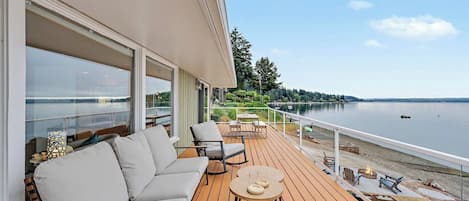 A deck with a sofa, chairs, and a table, overlooking a calm body of water.