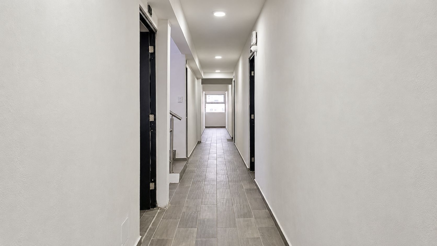 A corridor with white walls, a tiled floor, and doors on both sides.