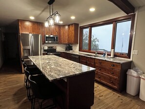 A kitchen with wooden cabinets, a stainless steel refrigerator, a microwave, a stove, a large island with bar stools, and a window with a view. - Stupendous Lake Ida Home on the Water and close to Carlos Creek Winery. Lic2061 (Alexandria)